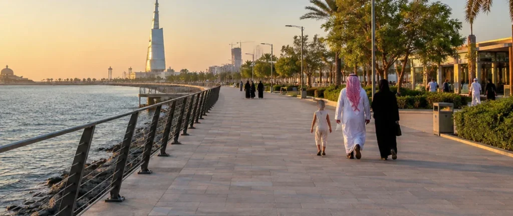 Saudi family walking the Jeddah Corniche seaside promenade at sunset with the city skyline behind them