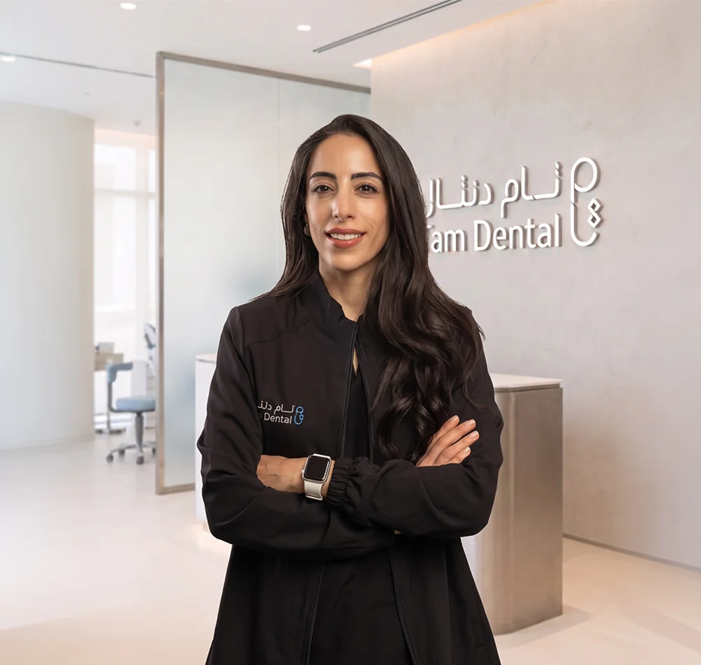 Dr. Dina Husein standing beside the Tam Dental reception sign in Jeddah