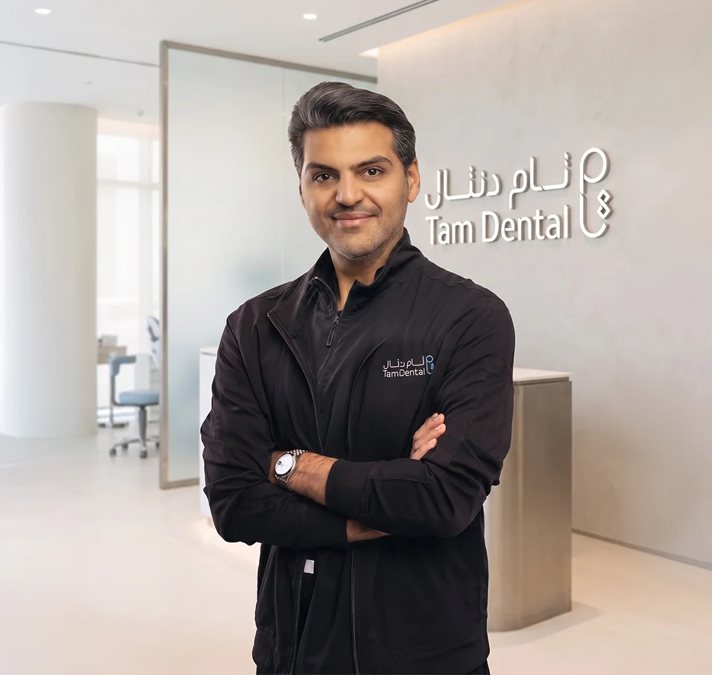 Dr. Rayan Bahabri standing beside the Tam Dental reception sign in Jeddah