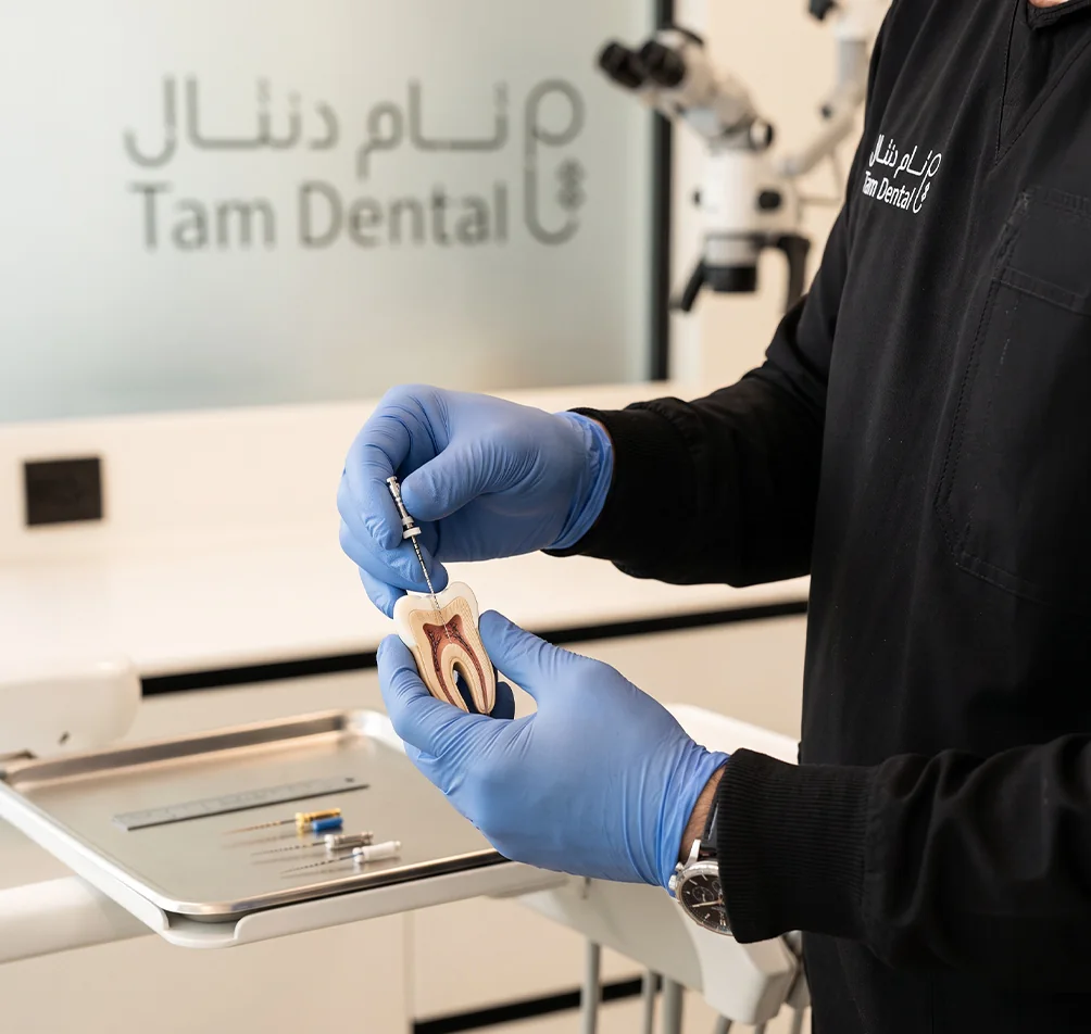 Endodontist holding a root canal tooth model beside a dental microscope at Tam Dental in Jeddah